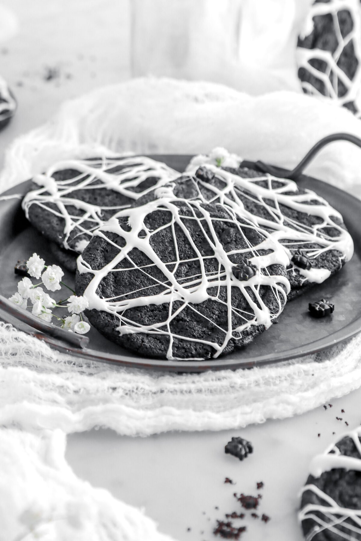 close up of spider web cookie on metal tray with white flowers beside.