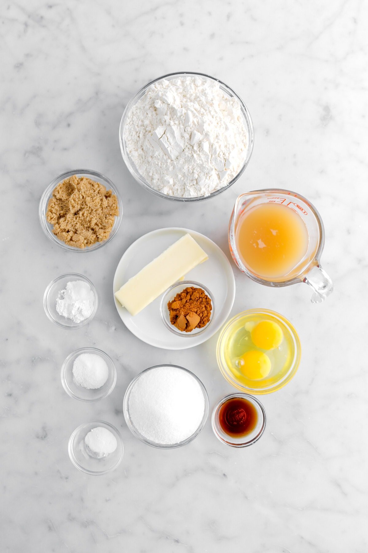 flour, brown sugar, apple cider, butter, ground spices, baking powder, baking soda, granulated sugar, vanilla, and salt on marble surface.