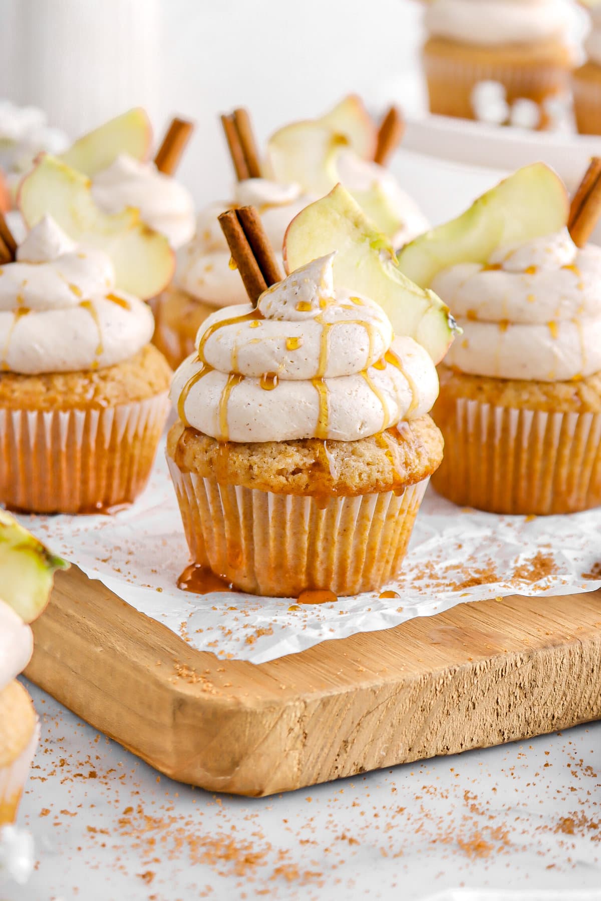 cupcakes on wood board with piped frosting, cinnamon stick, and an apple slice on each cupcake.