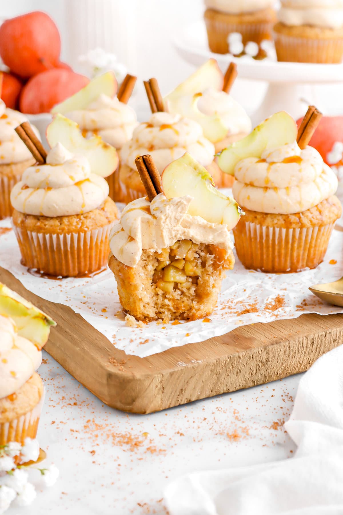 angled image of four cupcakes on wood board with one cupcake missing a bite and apples behind.