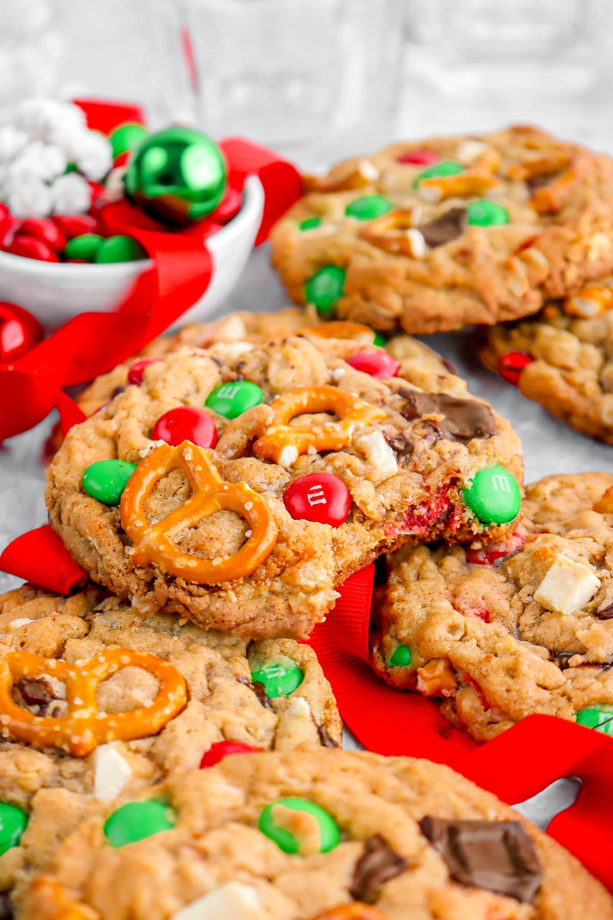 close up image of monster cookie with bite missing, a red ribbon, bowl of M&M's, and mini ornaments behind.