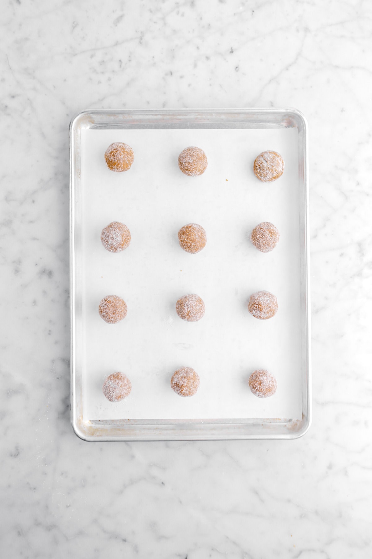 twelve cookie dough balls on parchment lined sheet pan.