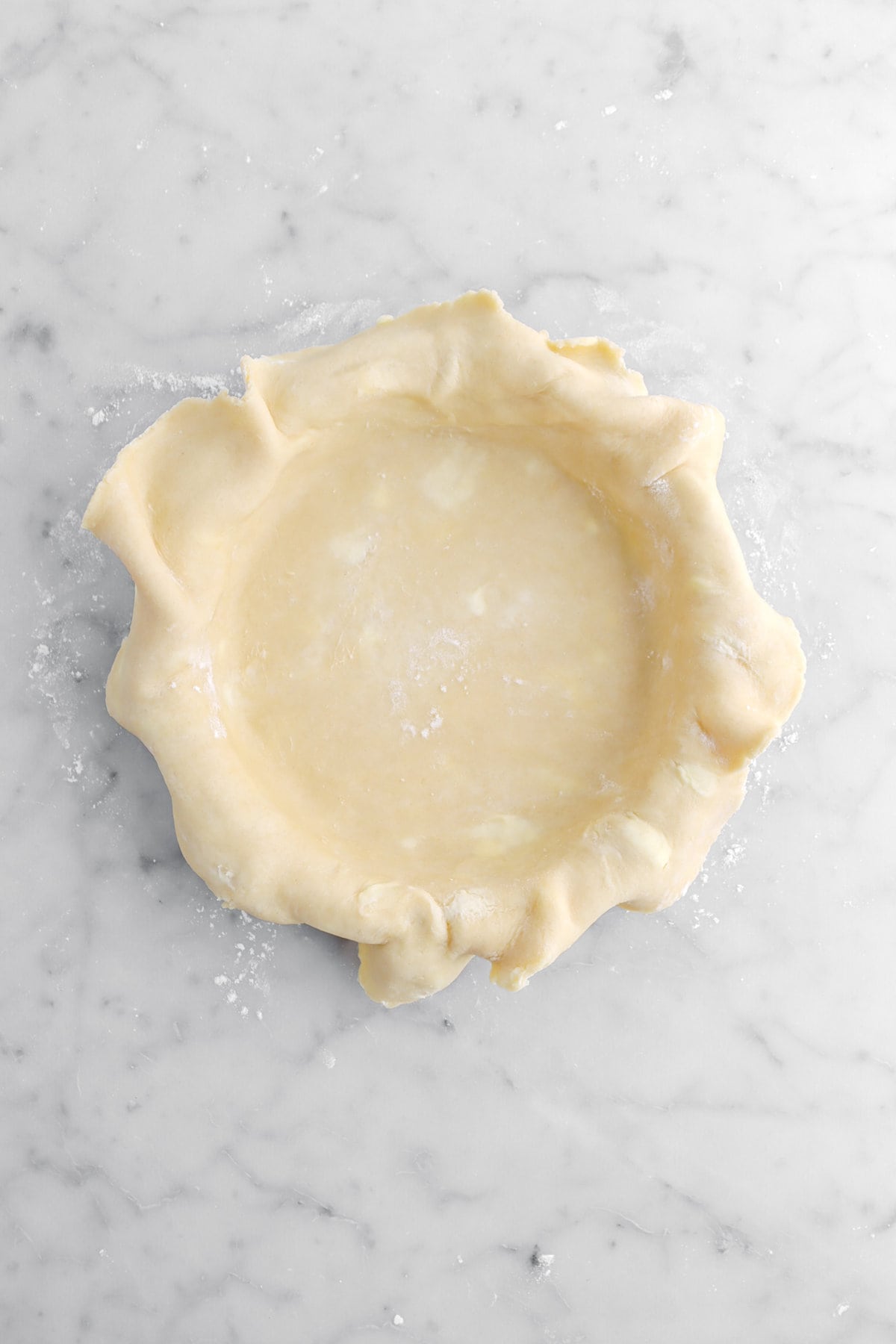 pie dough fitted to pie pan with excess hanging off edges.