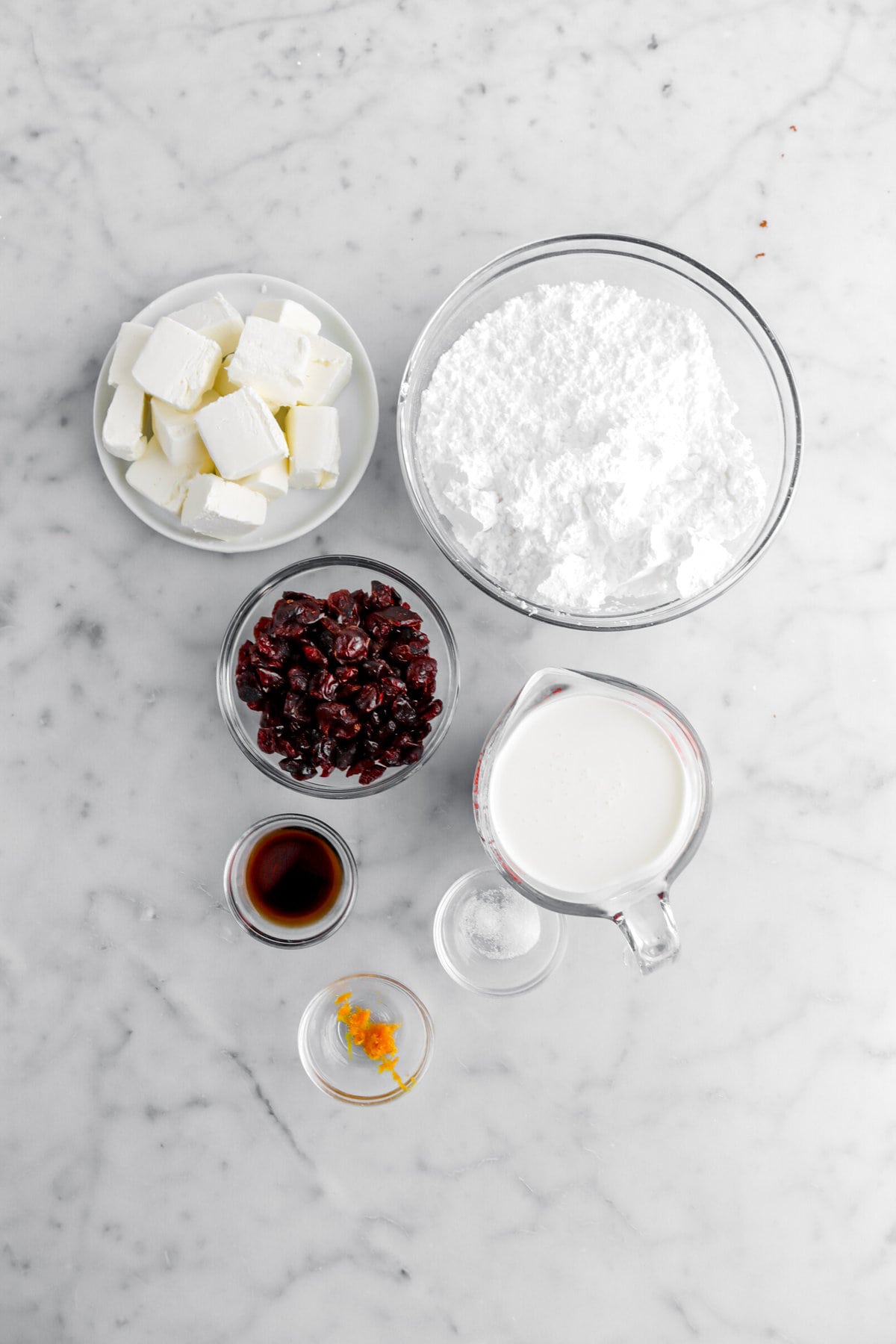 cream cheese, powdered sugar, dried cranberries, vanilla, heavy cream, salt, and orange zest on marble surface.