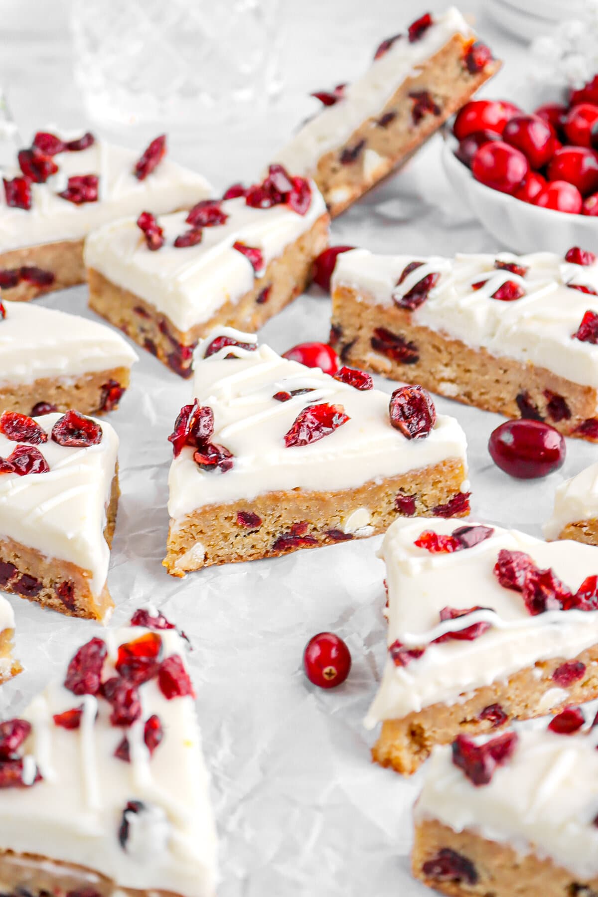 angled image of cranberry white chocolate blondies on parchment paper with fresh cranberries around.