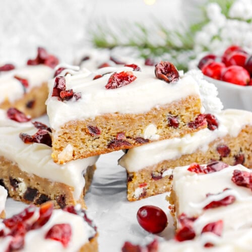 close up of three cranberry bliss bars piled on parchment paper.