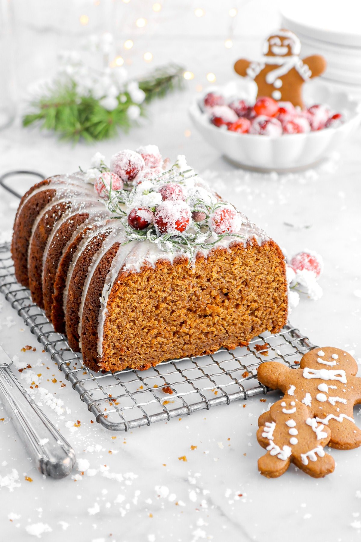 angled close up of gingerbread loaf cake on wire tray with two gingerbread cookies beside.