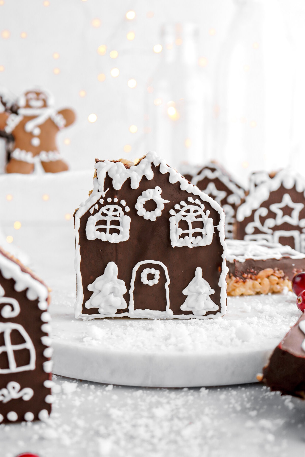 image of decorated gingerbread house rice krispie treat with fairy lights behind and more rice krispie treats around.