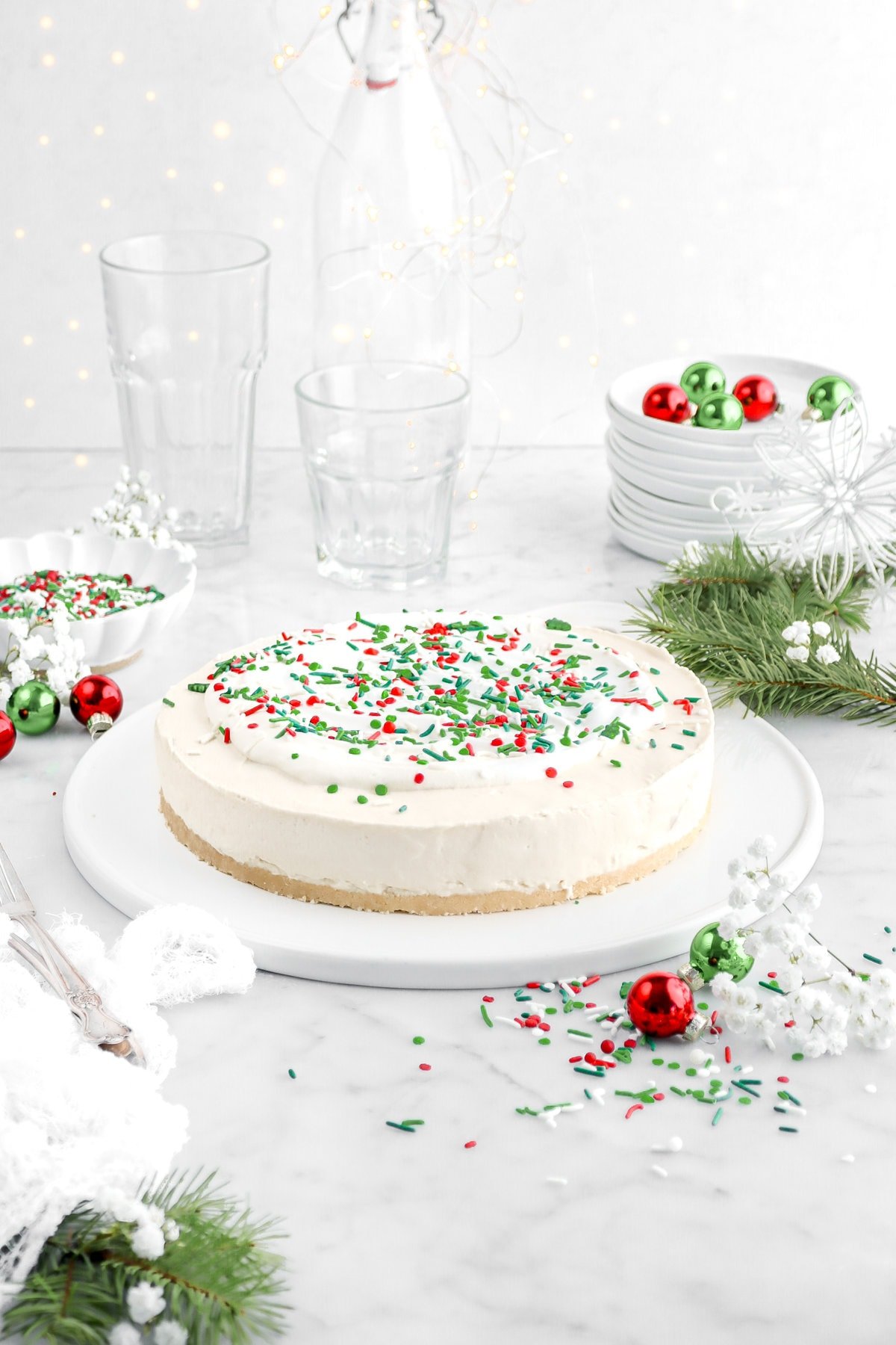 cheesecake on serving tray with red, white, and green sprinkles on top with greenery and red and green ornaments around.