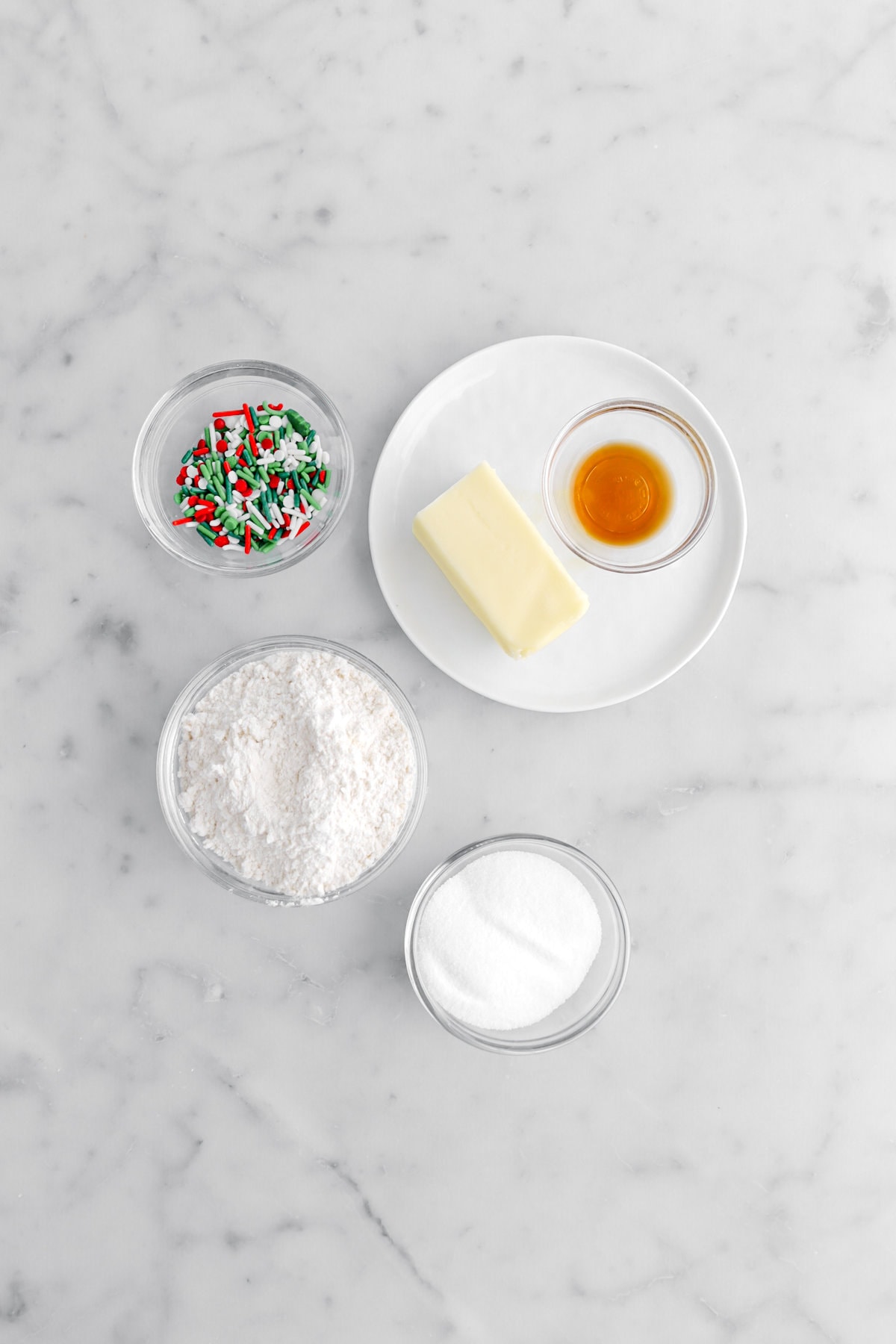 sprinkles, butter, vanilla, flour, and sugar on marble surface.