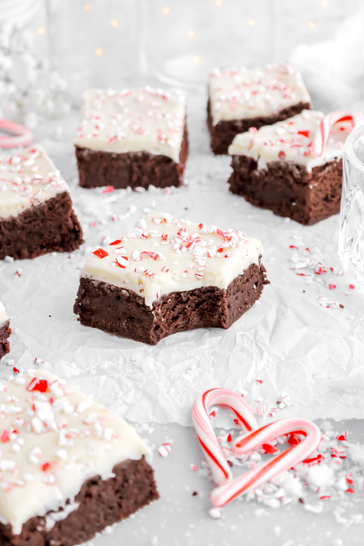close up image of peppermint bark brownie with bite missing with more brownies around on parchment paper.