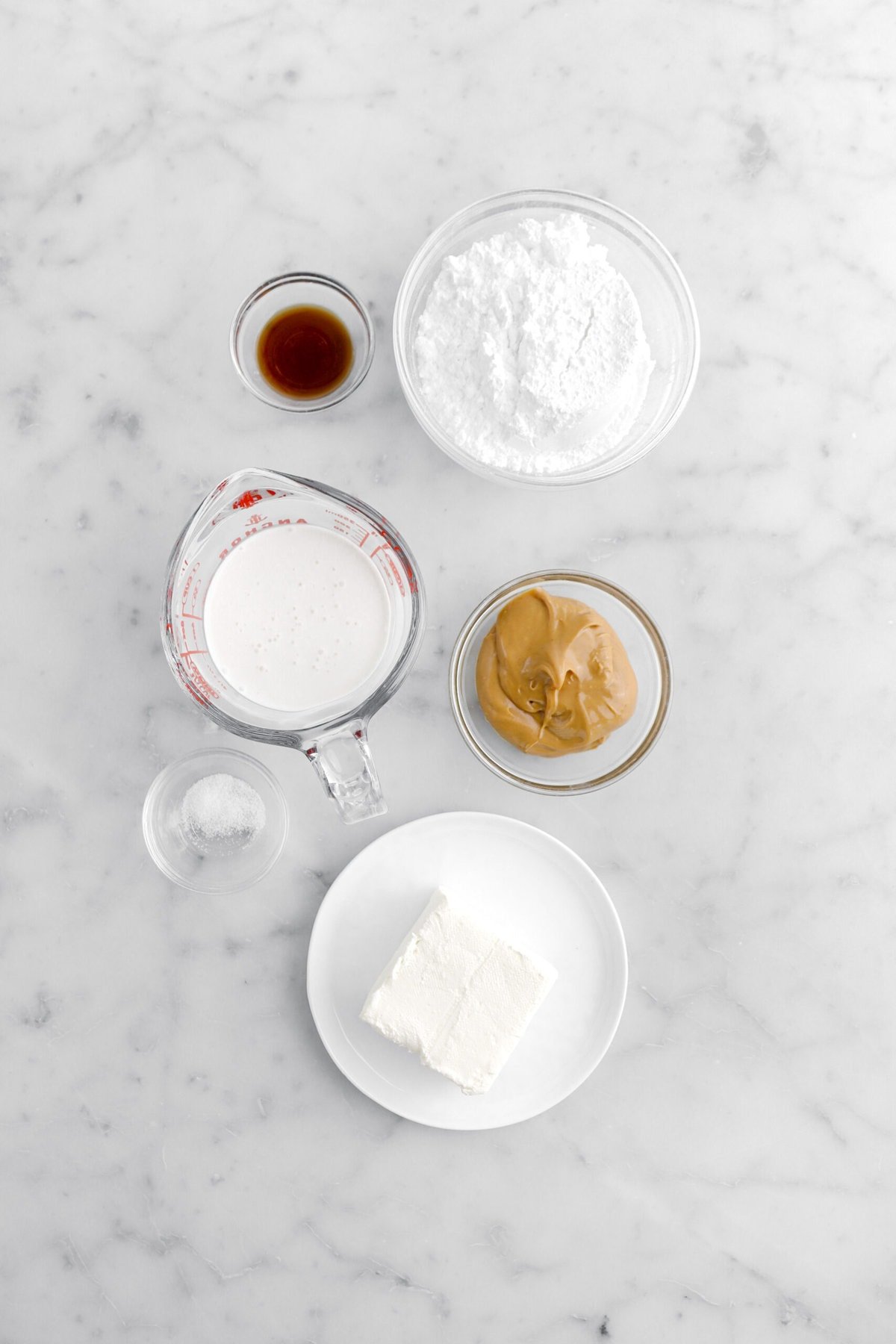 vanilla, powdered sugar, cream, peanut butter, salt, and cream cheese on marble surface.
