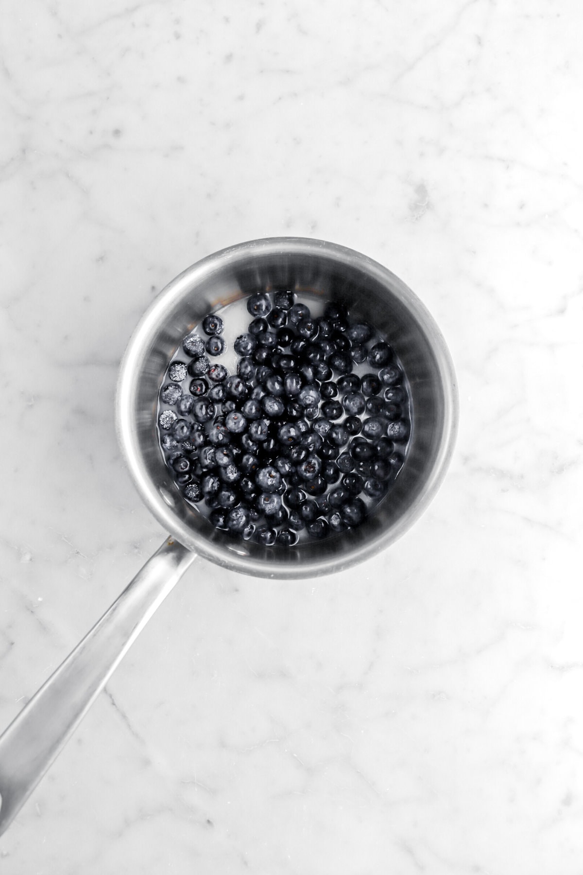pot of blueberries, sugar, and water on marble surface.