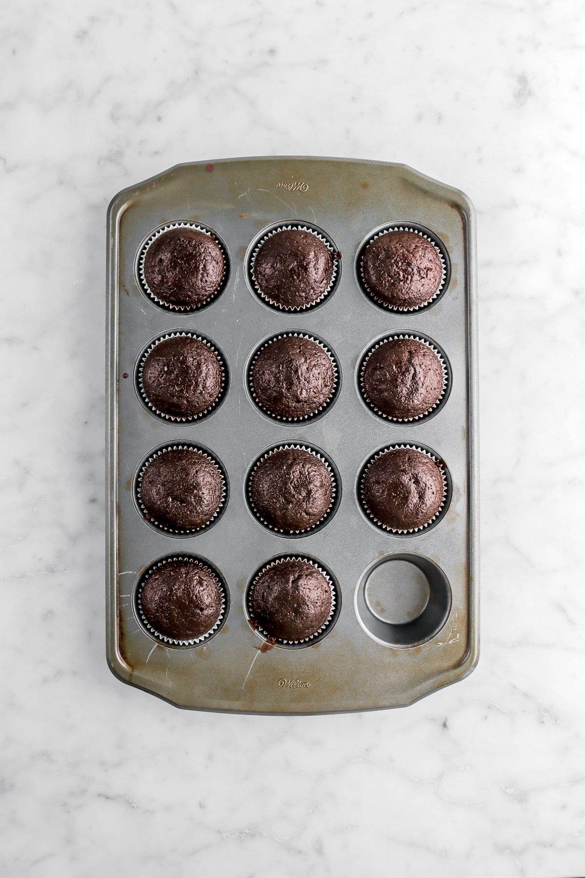 11 baked chocolate cupcakes in muffin pan.