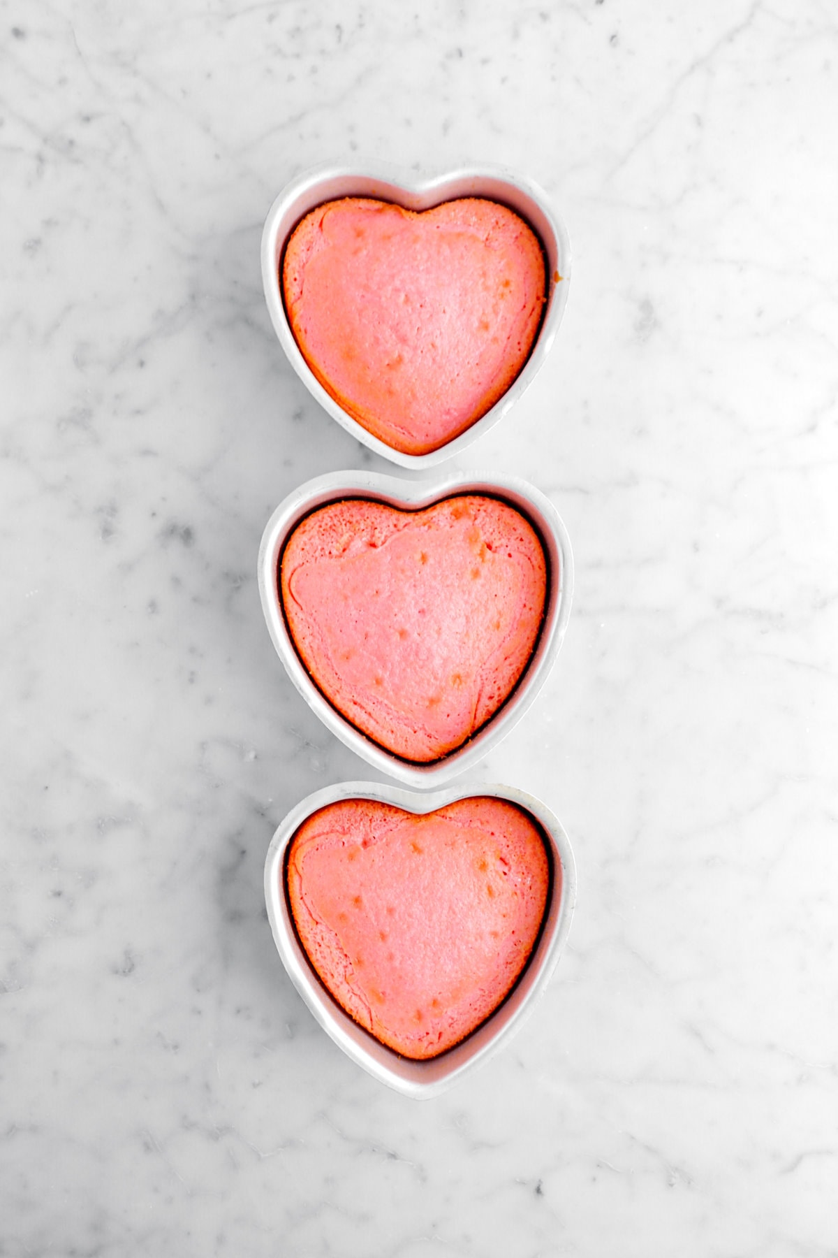 three baked pink cake layers in heart shaped pans.