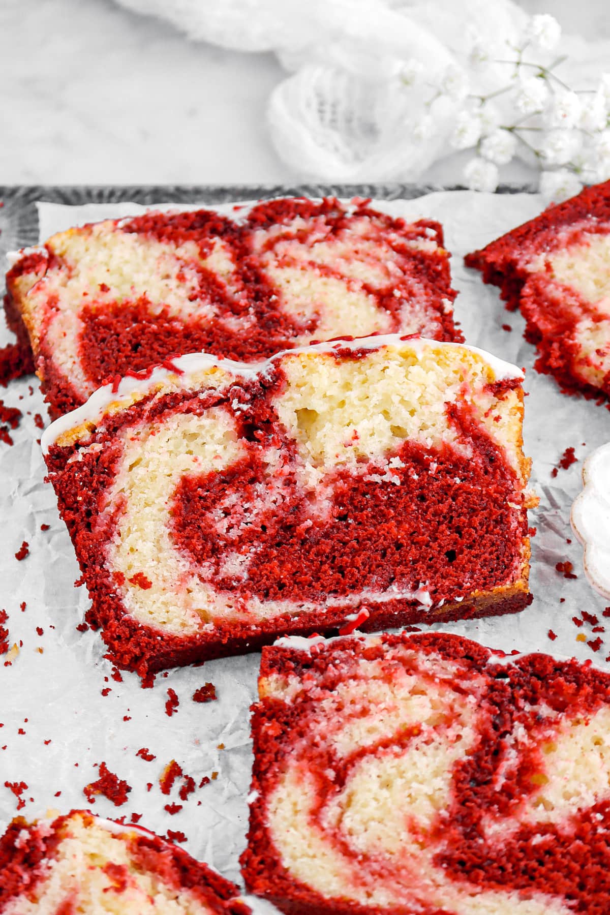 angled close up of slice of red velvet swirl loaf cake on parchment paper lined sheet pan.