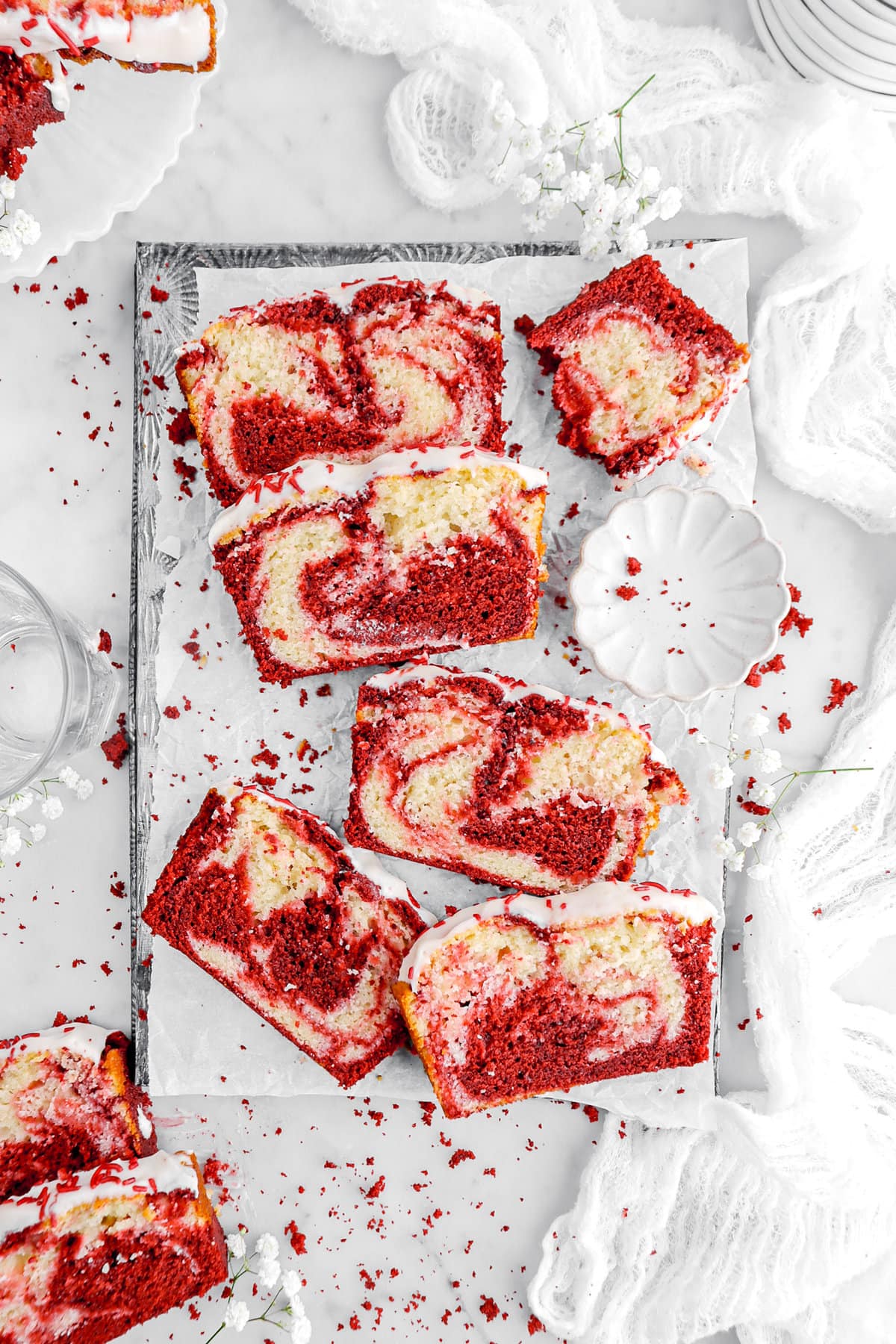 overhead image of 5 slices of red velvet swirl cake on parchment lined sheet pan with scalloped bowl and half piece of cake.