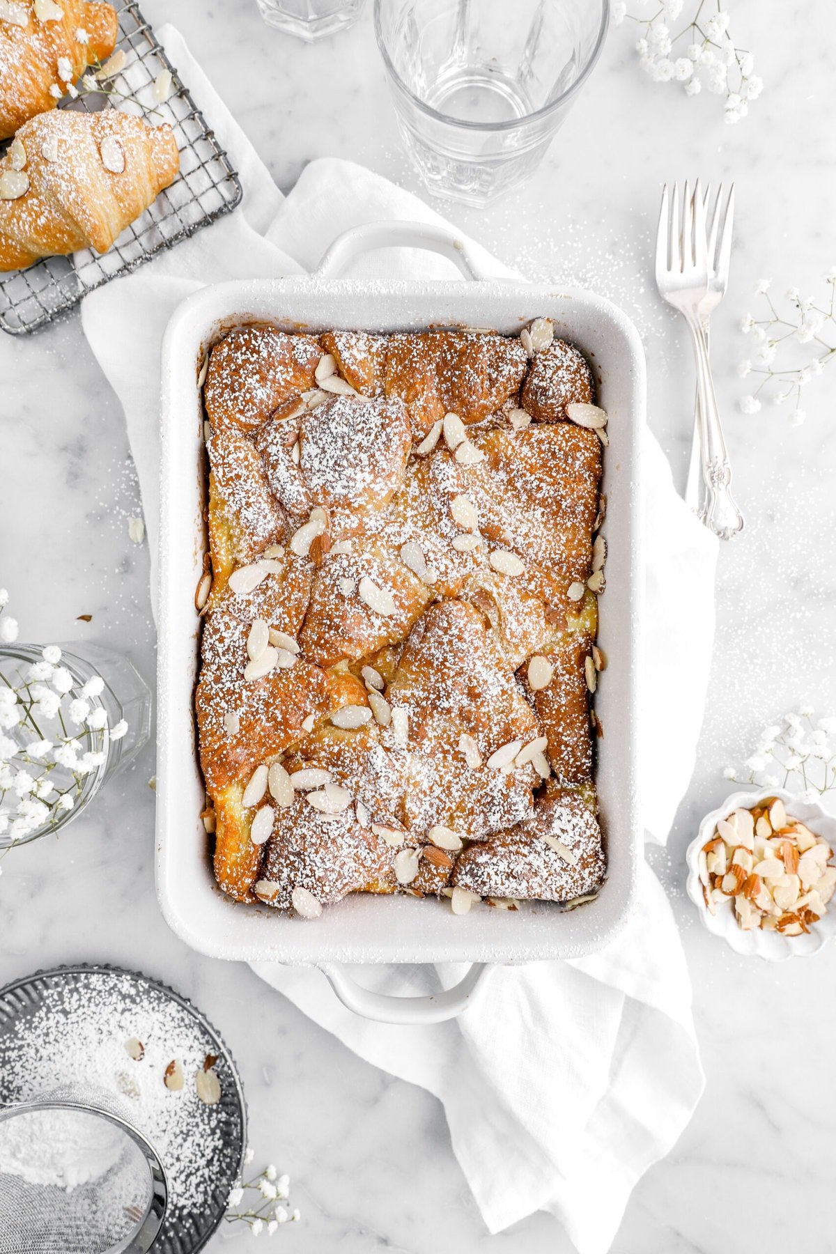 overhead image of vanilla croissant bread pudding on top of a white napkin with forks and flowers around.