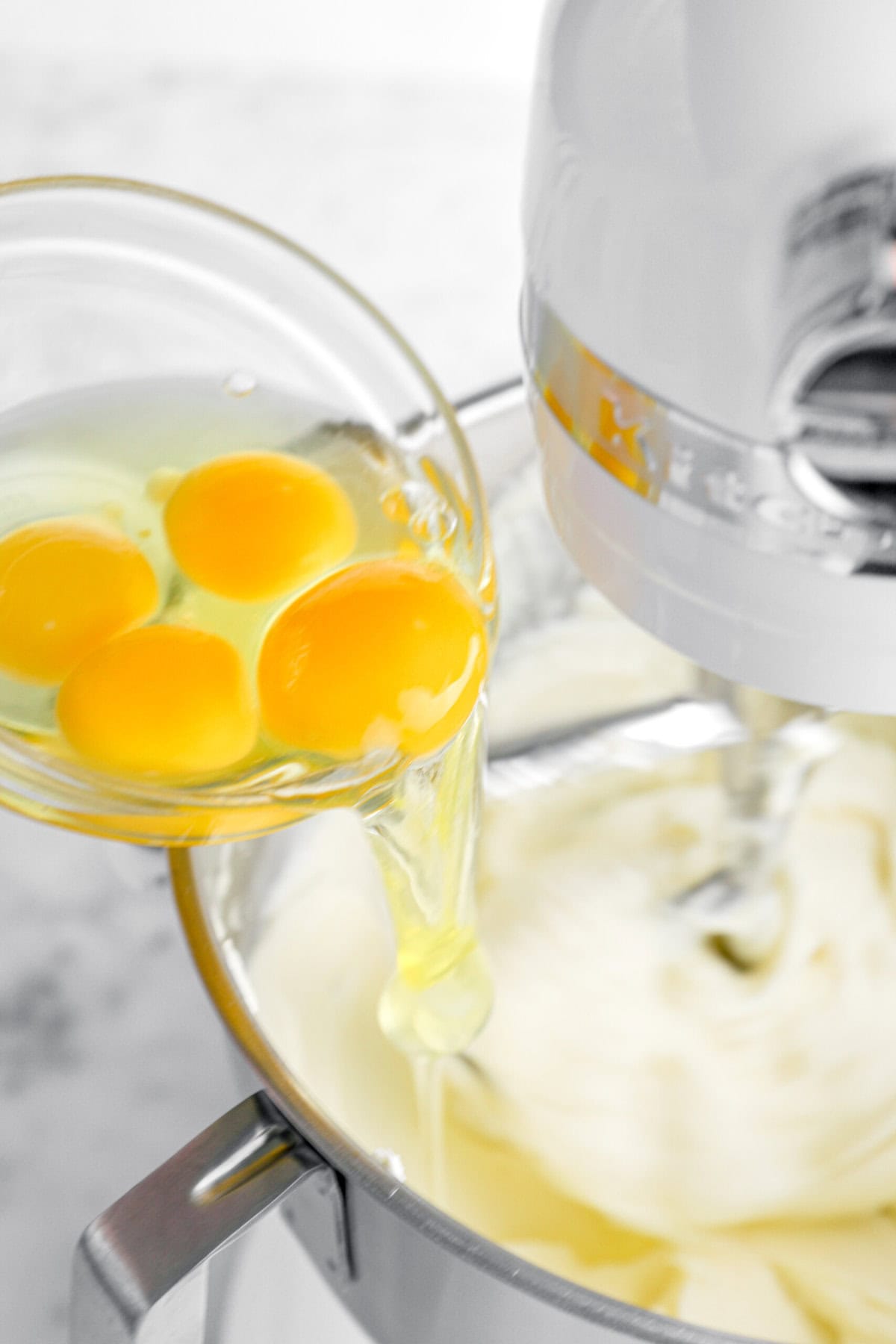 eggs being added to cream cheese in mixer.
