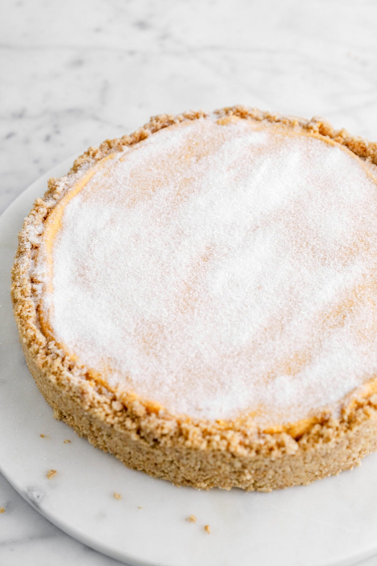 pumpkin cheesecake with a graham cracker crust and granulated sugar on top.