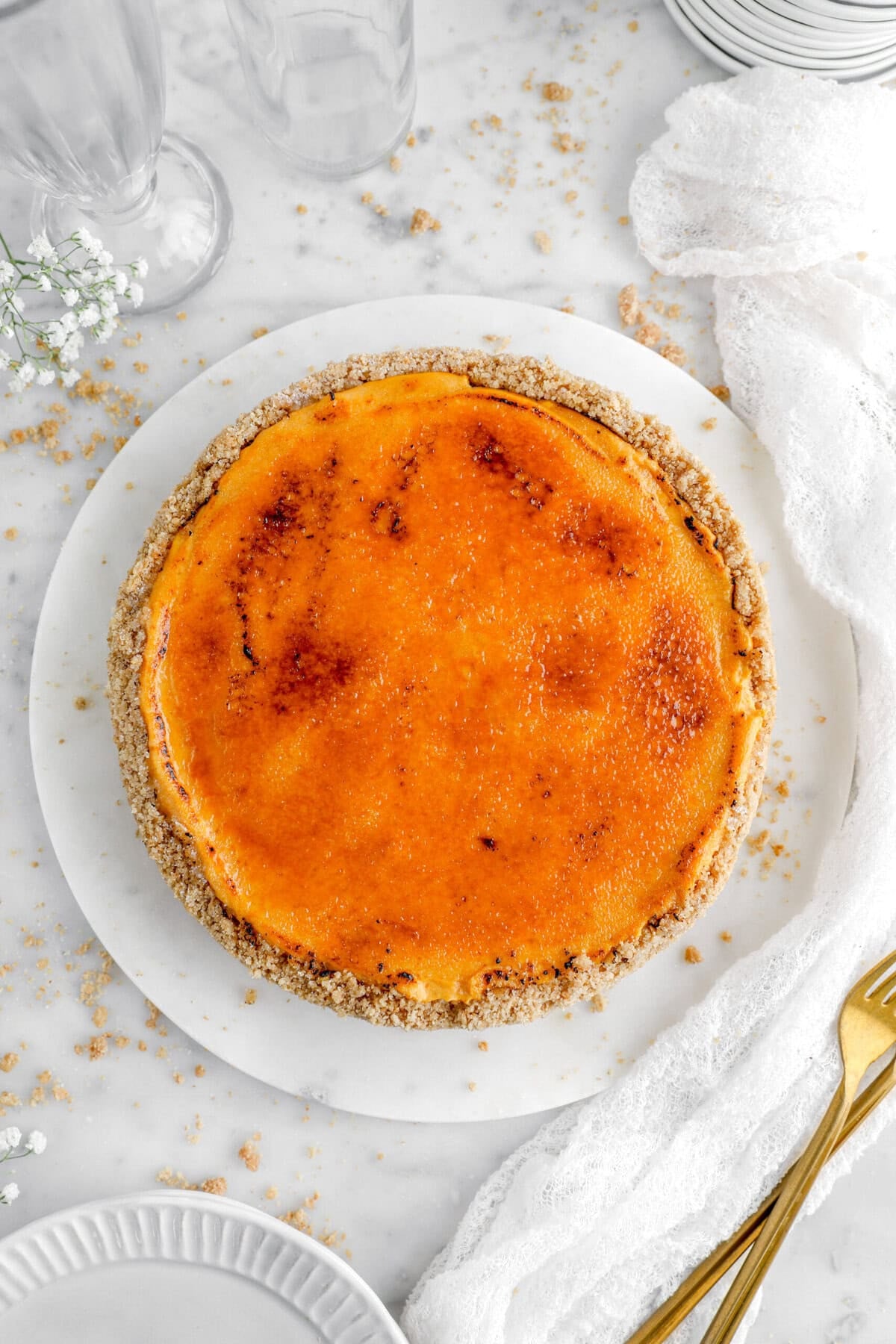 Delicious caramelized cheesecake on a white plate with crumbs and gold fork.