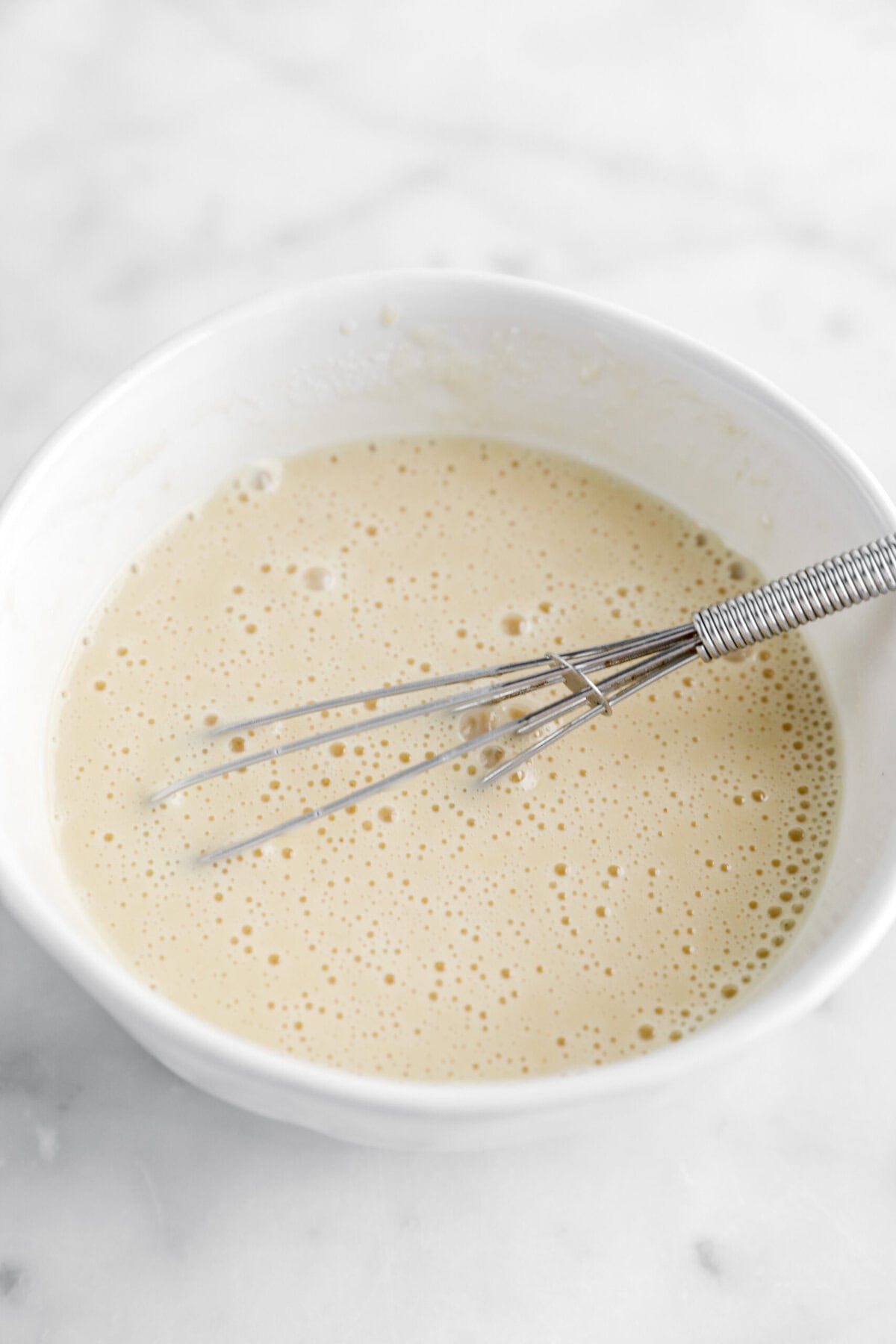 wet ingredients whisked in white bowl with whisk.