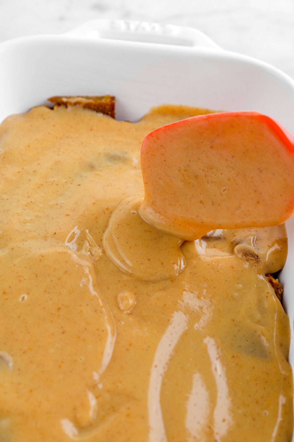 pumpkin custard being spread over pumpkin bread in white casserole.