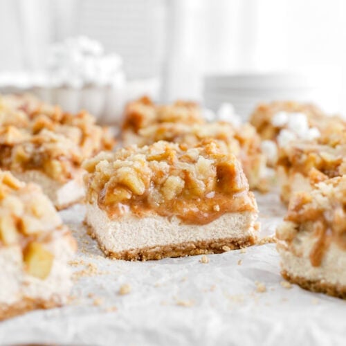 apple cheesecake bars on wood surface lined with parchment.
