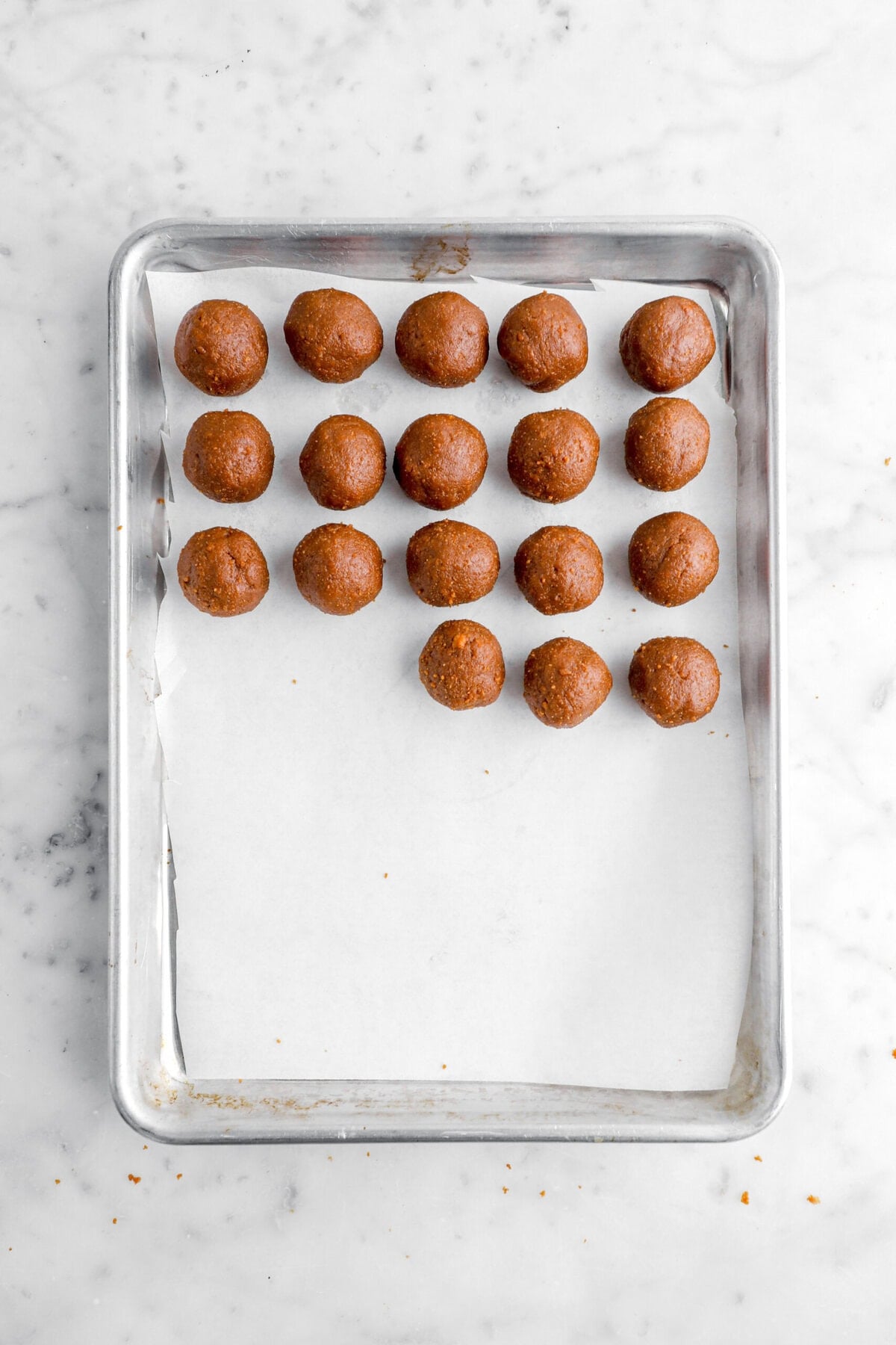 18 cookie dough balls on lined sheet pan.