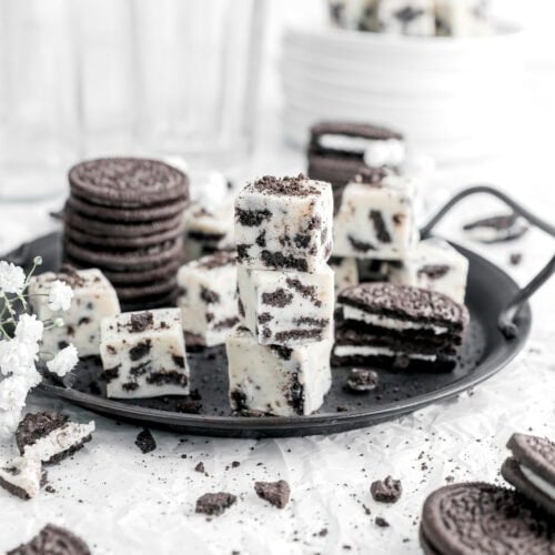 three stacked oreo fudge squares on black plate with more fudge and oreos around.